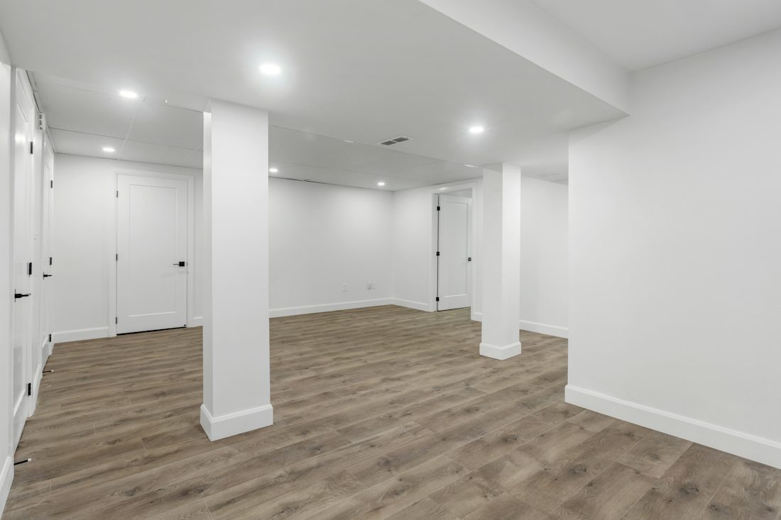 Finished basement room with white walls, recessed lights, and wood-look floor