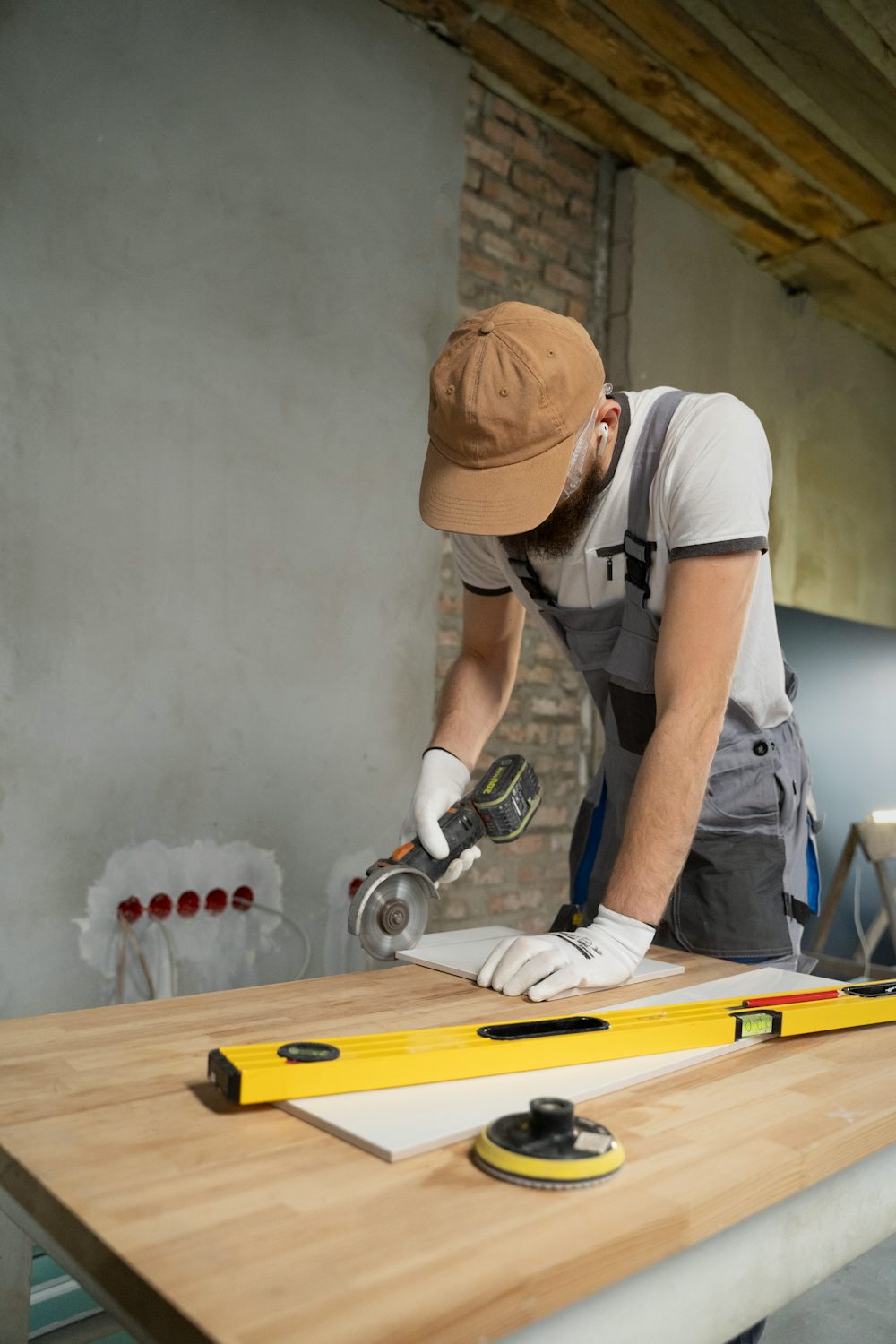 Worker in a cap and overalls cutting tile with an angle grinder